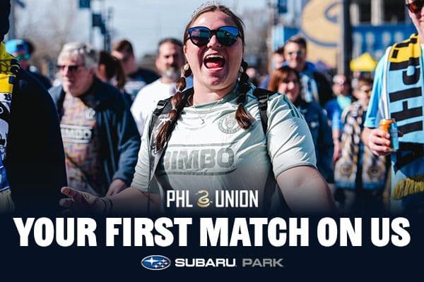 Enthusiastic soccer fans walk together, one wearing a Philadelphia Union shirt and sunglasses, smiling. Text reads "Your First Match On Us." Subaru Park logo below.